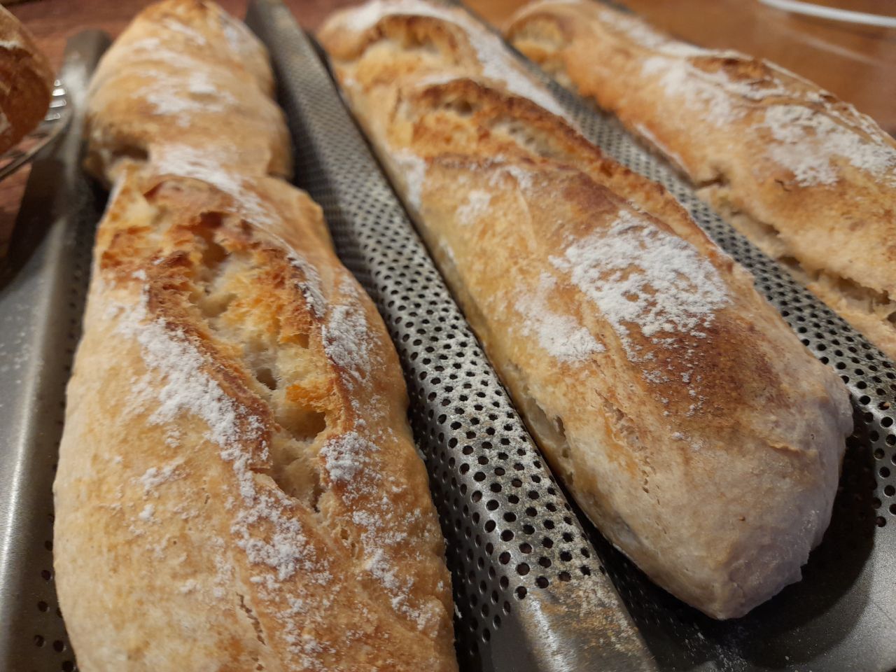 Drei knusprige Baguettes liegen auf einem Metallregal, frisch gebacken und sehr lecker.