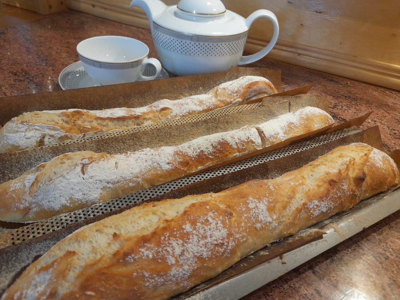 Auf einem Metallregal befinden sich drei lange, knusprige Baguettes, die gut verträglich und köstlich sind.